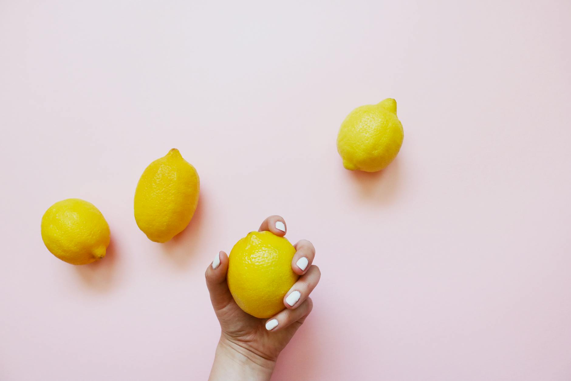 A hand holding a fresh lemon on a soft pink background, symbolizing renewal and self-care