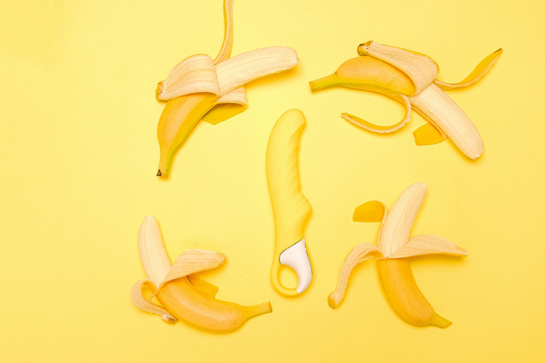 Yellow silicone vibrator surrounded by peeled lemons on a yellow background, symbolizing pleasure and freshness