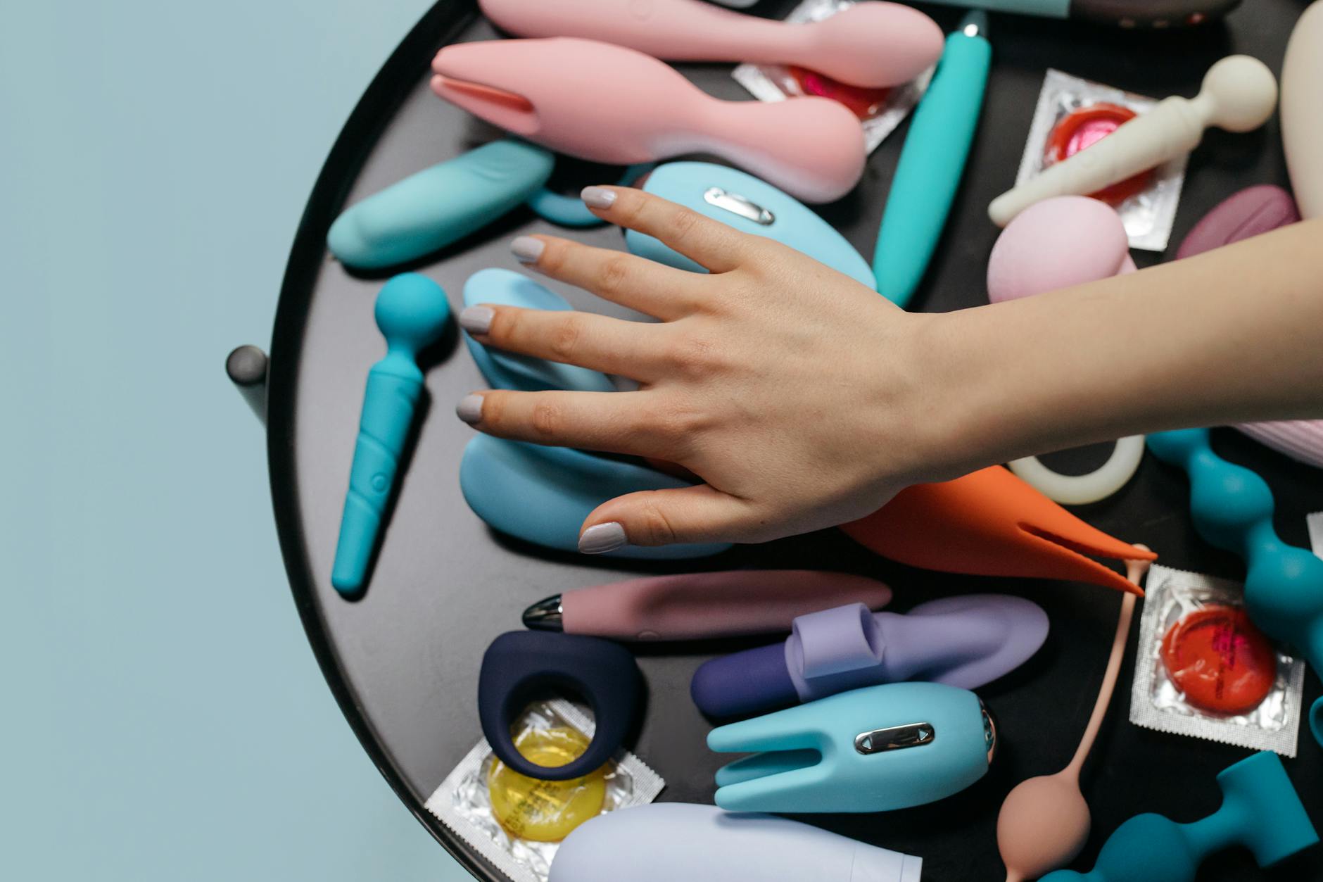Hand reaching over a colorful collection of vibrators on a table