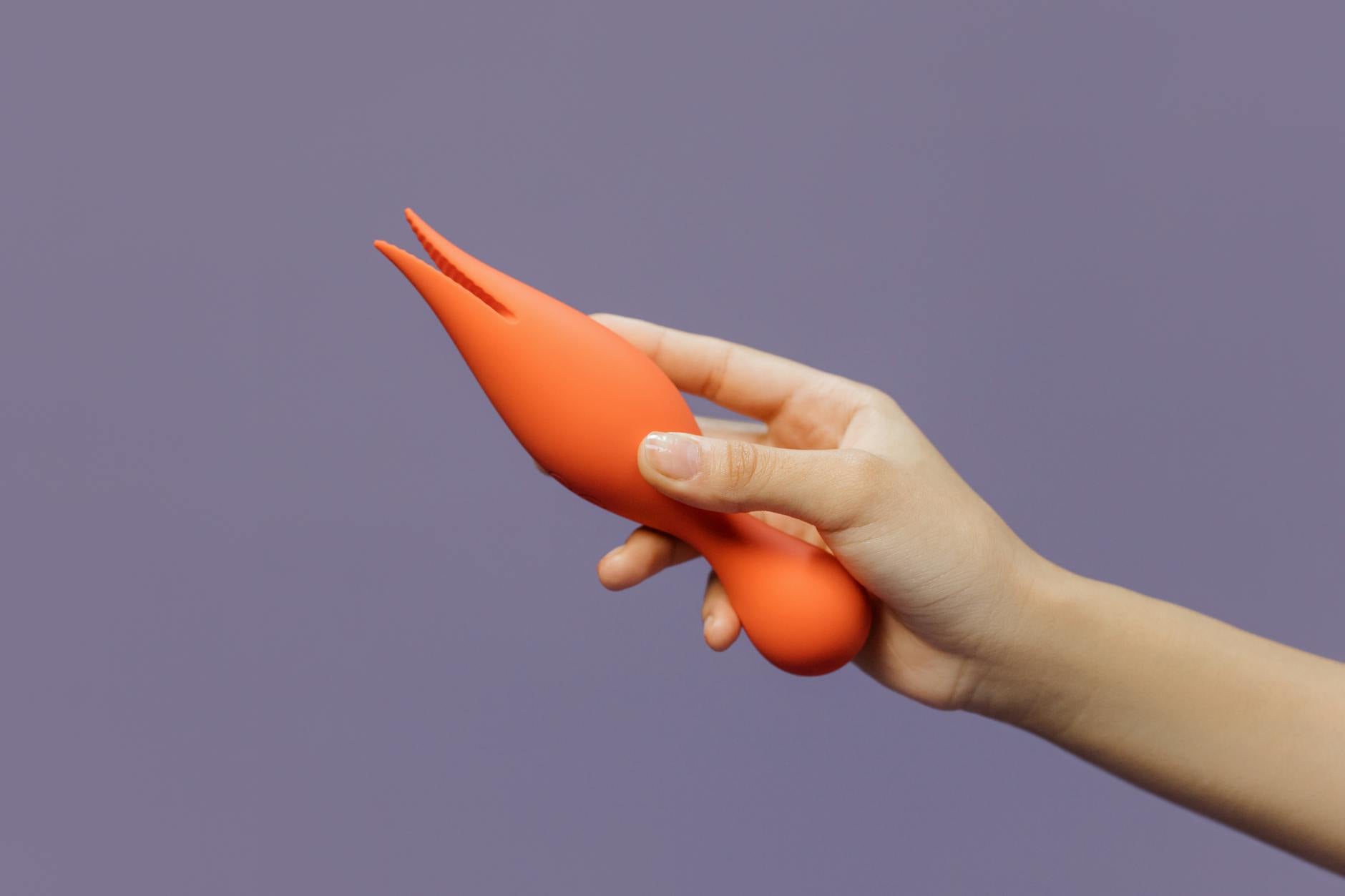 Hand holding a bright yellow lemon vibrator against a minimalist purple backdrop